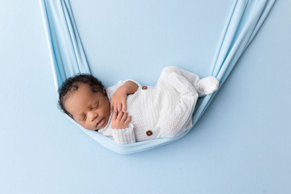 Peaceful baby sleeping in light blue fabric sling against pastel background.