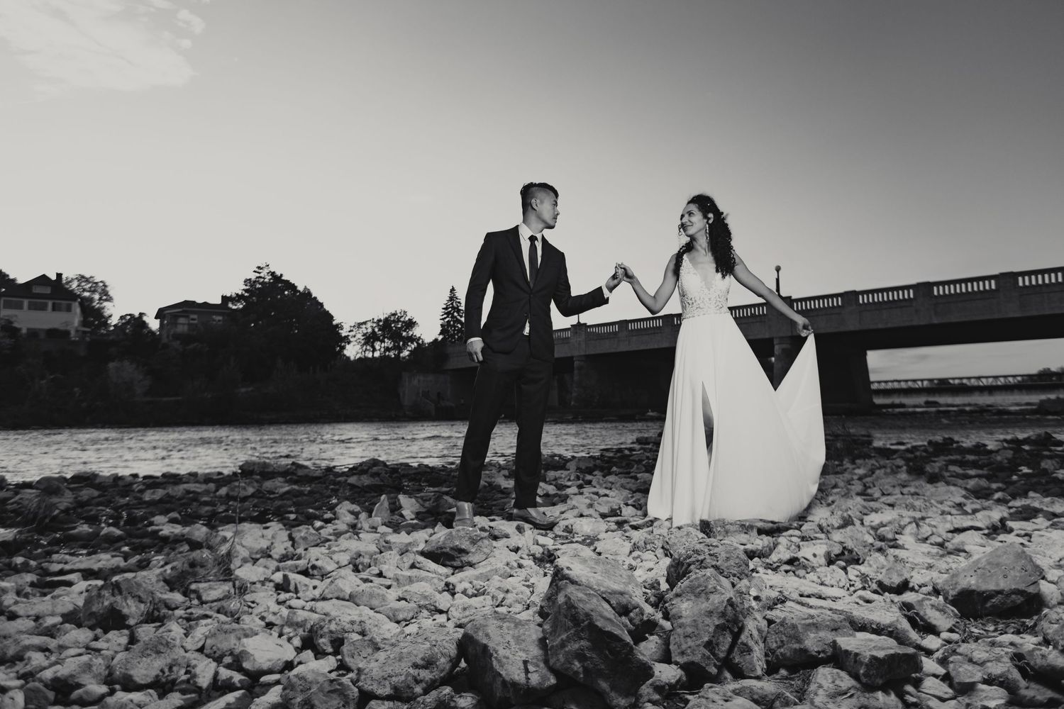 Bride and Groom holding hands beside a flowing lake and bridge