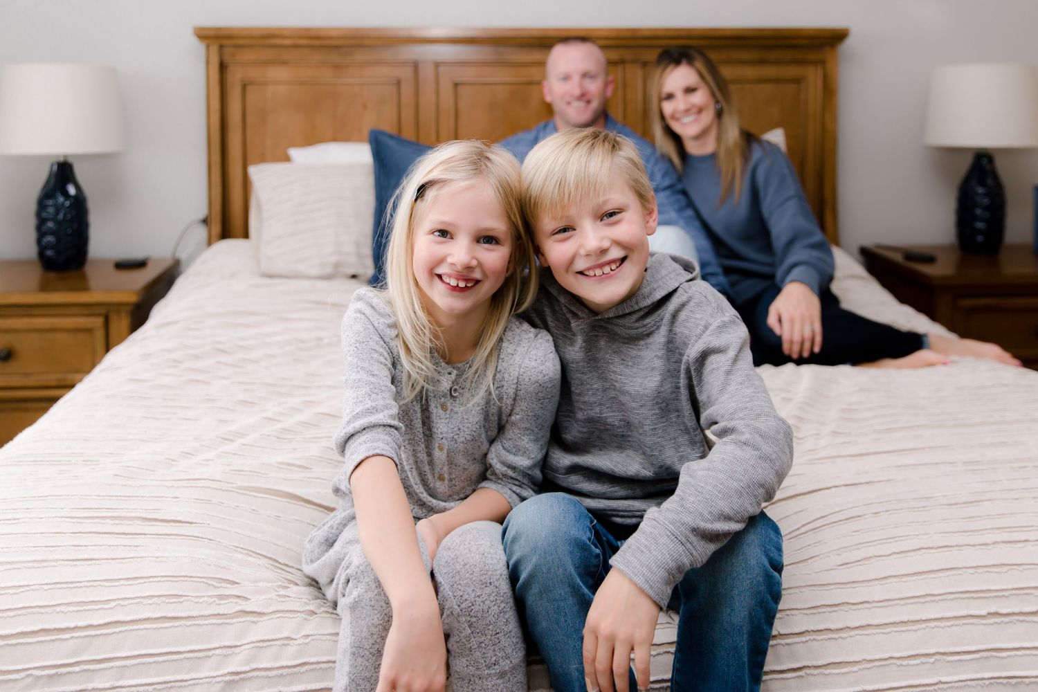 Owen and Charli sitting on the edge of the bed with mom and dad blurred in the background smiling.