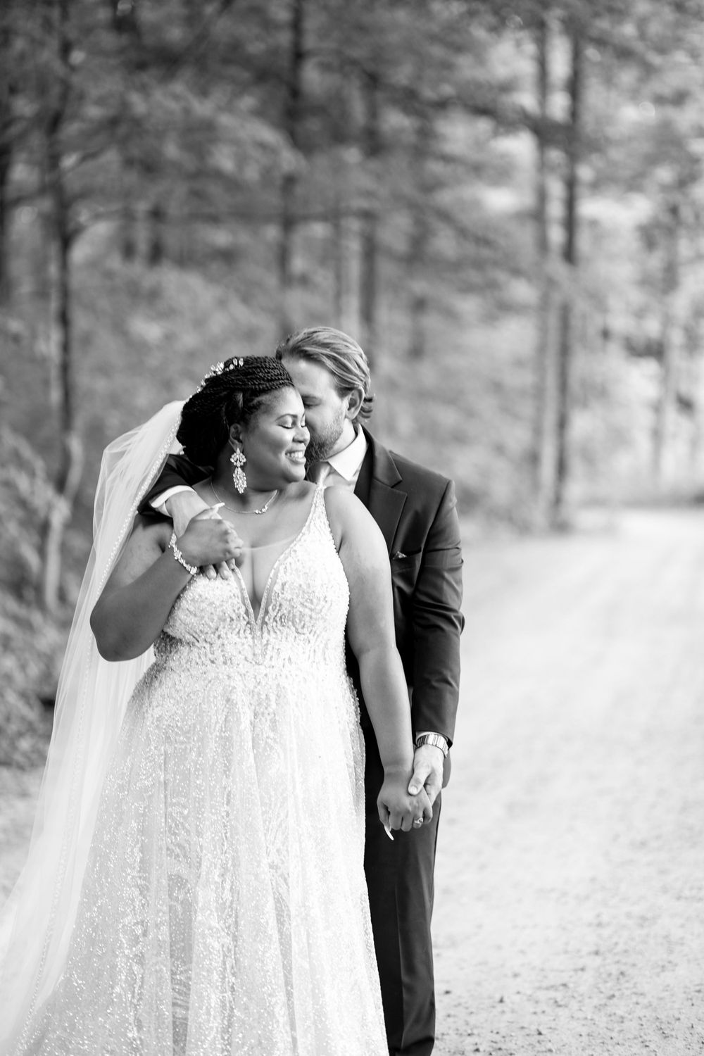 Black and white romantic wedding portrait on a tree-lined path.