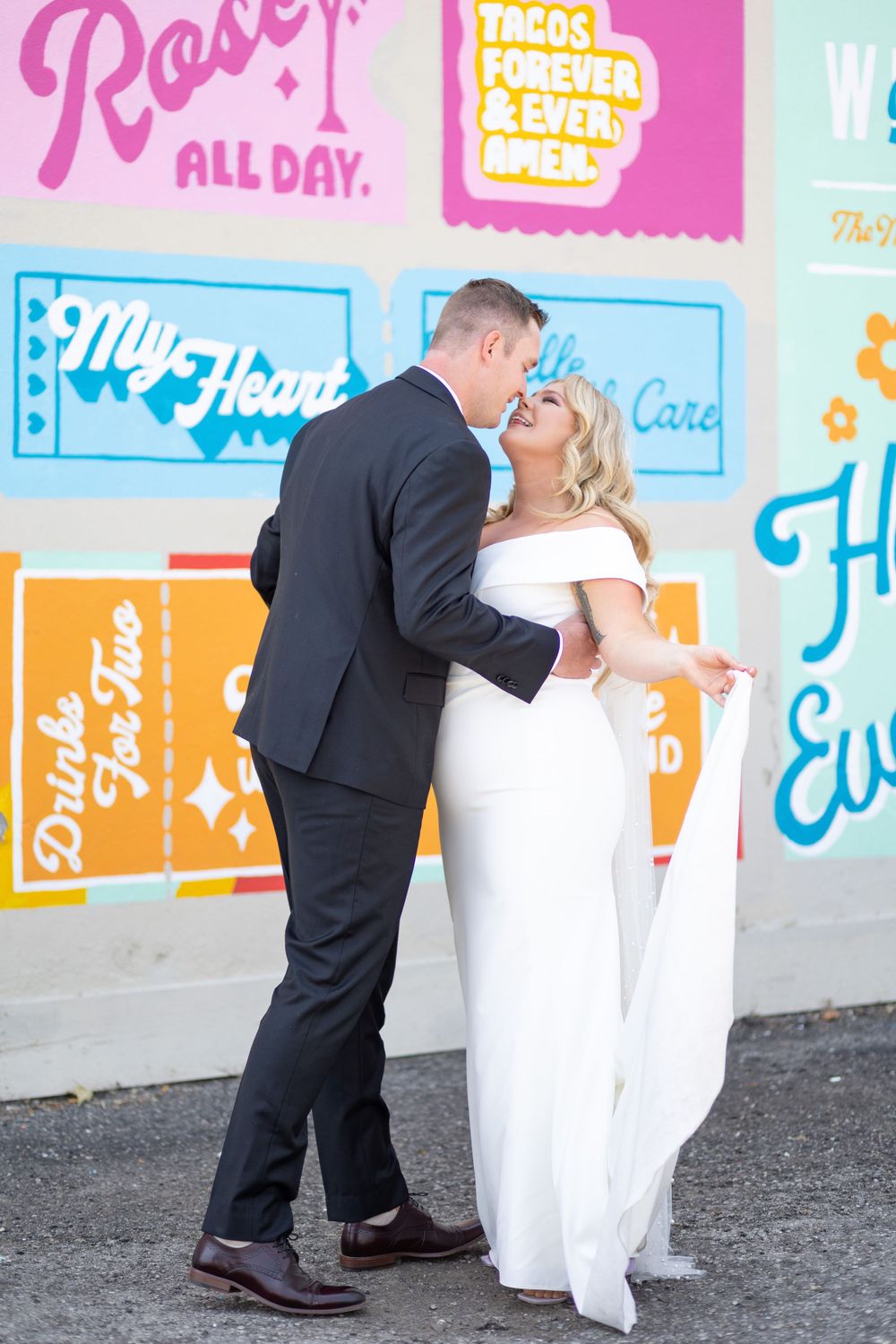 Newlyweds sharing romantic moment against colorful mural wall.