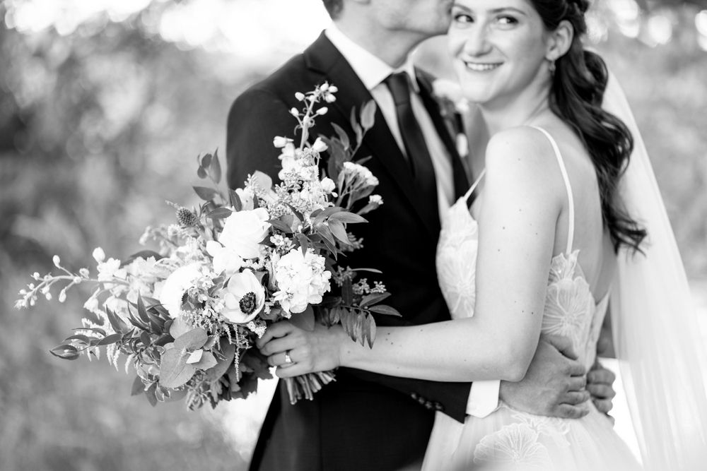 A romantic black and white wedding photo showing a couple embracing while holding a beautiful floral bouquet.