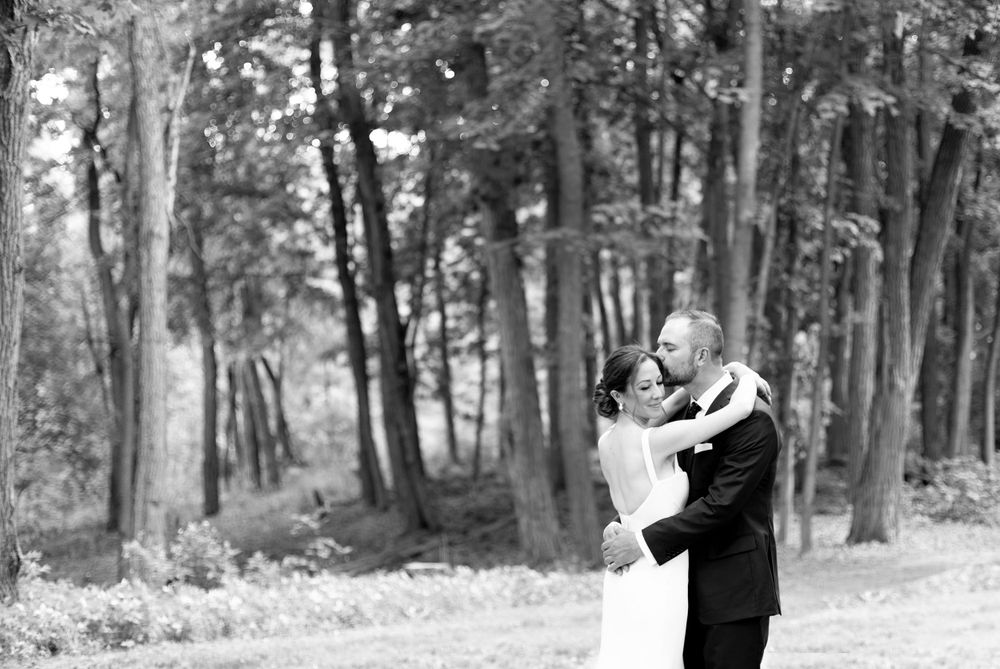 A romantic black and white photo of newlyweds embracing in a serene wooded setting.