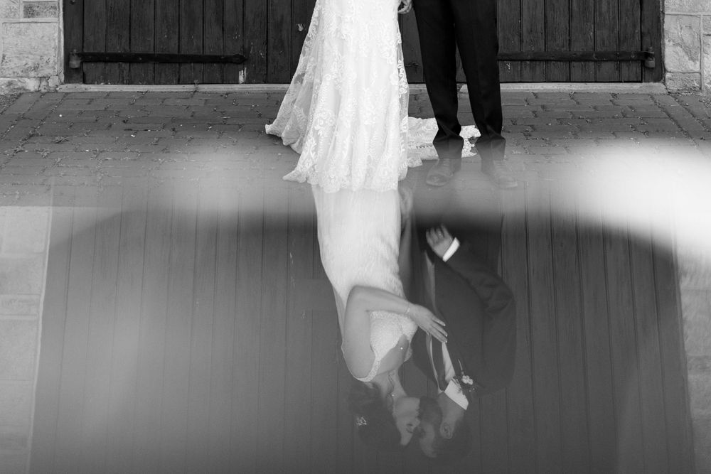 Artistic black and white photo showing the reflection of a bride and groom's feet on a wooden floor.
