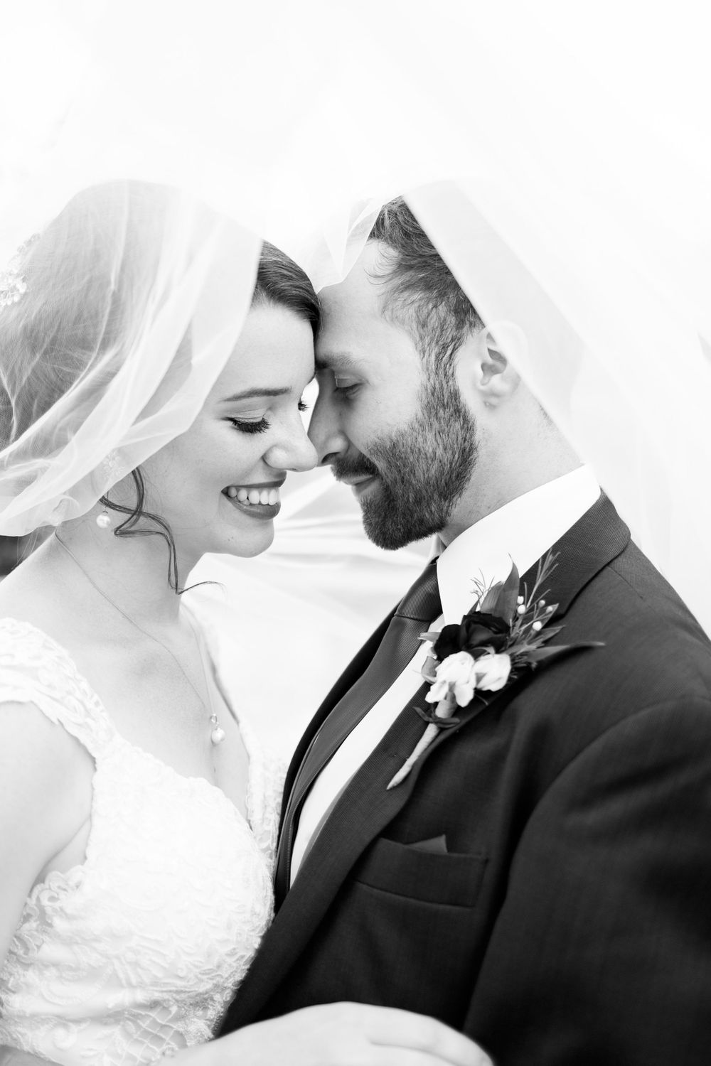 Intimate black and white portrait of newlyweds sharing tender moment under bridal veil.