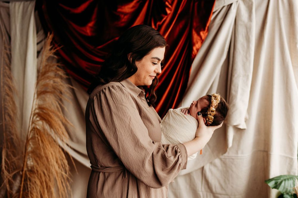 Gentle interaction with swaddled newborn against draped fabric backdrop.