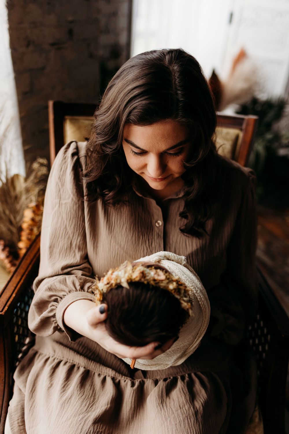 Newborn wearing crown rests peacefully in caregiver's arms during indoor portrait session.