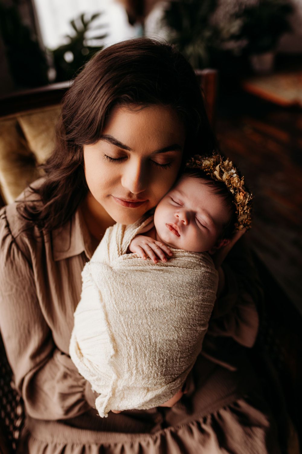 A tender moment between parent and swaddled sleeping newborn wearing a delicate floral crown.