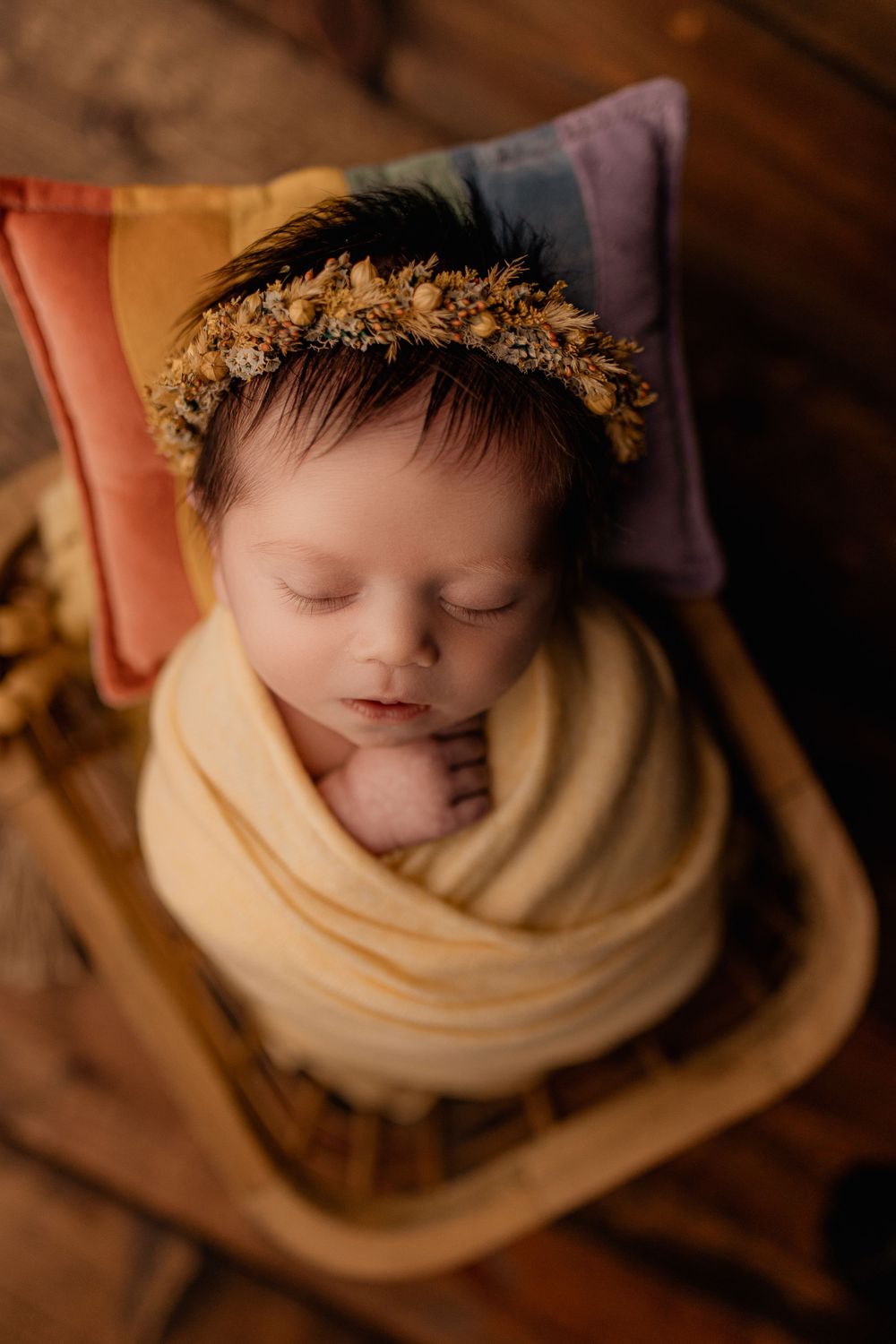 Overhead view of sleeping newborn with dried flower crown wrapped in cream fabric.