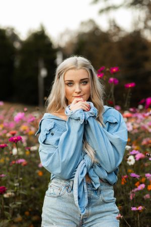 Blonde teenage girl in denim jacket posing in a colorful wildflower field.