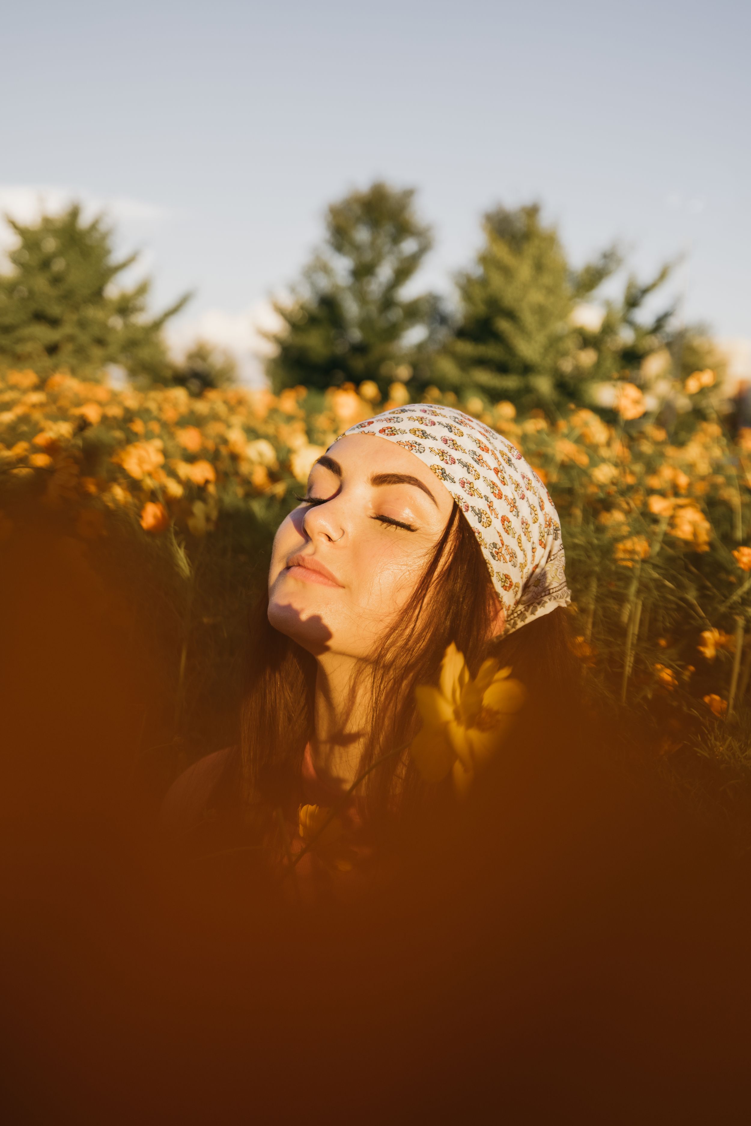 Young woman with closed eyes wearing a bandana headscarf surrounded by golden wildflowers.