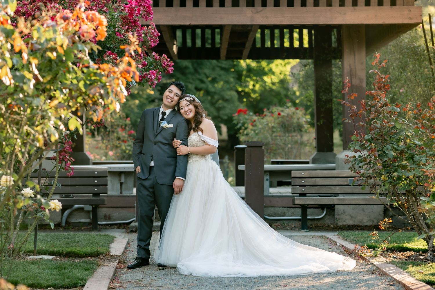 A couple poses under a wooden pergola surrounded by colorful autumn flowers.