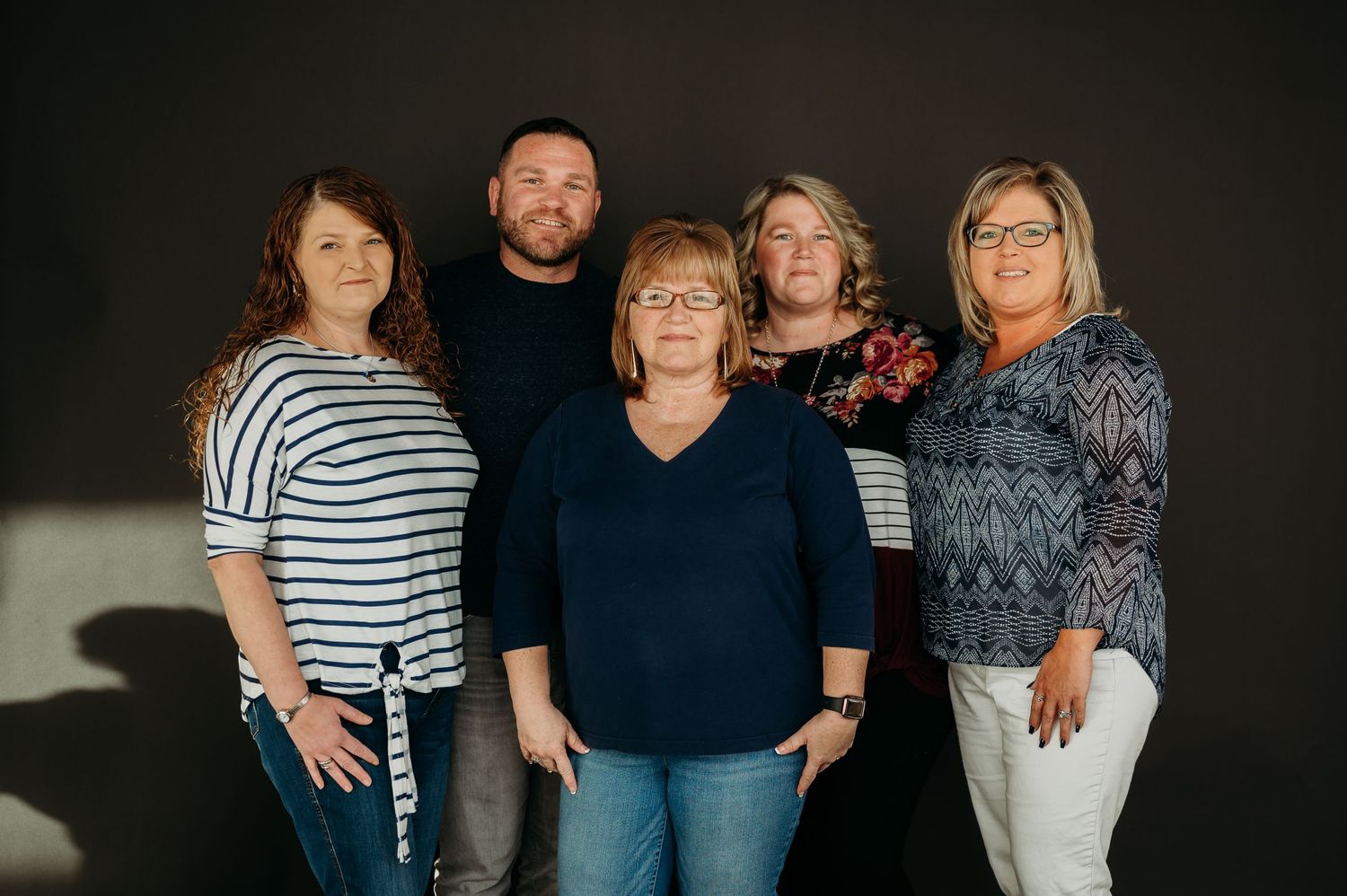 Group of five adults posing together for family portrait against dark background.