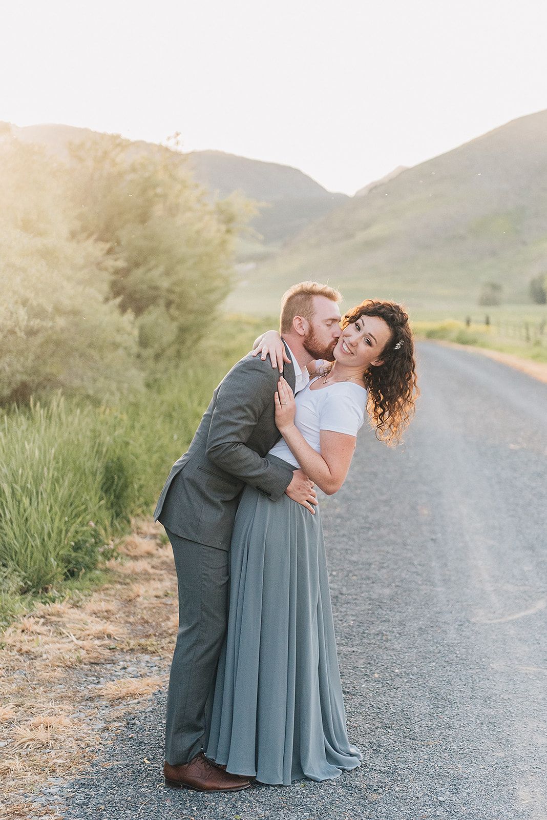 A playful couple sharing a romantic moment on a rural road at sunset.