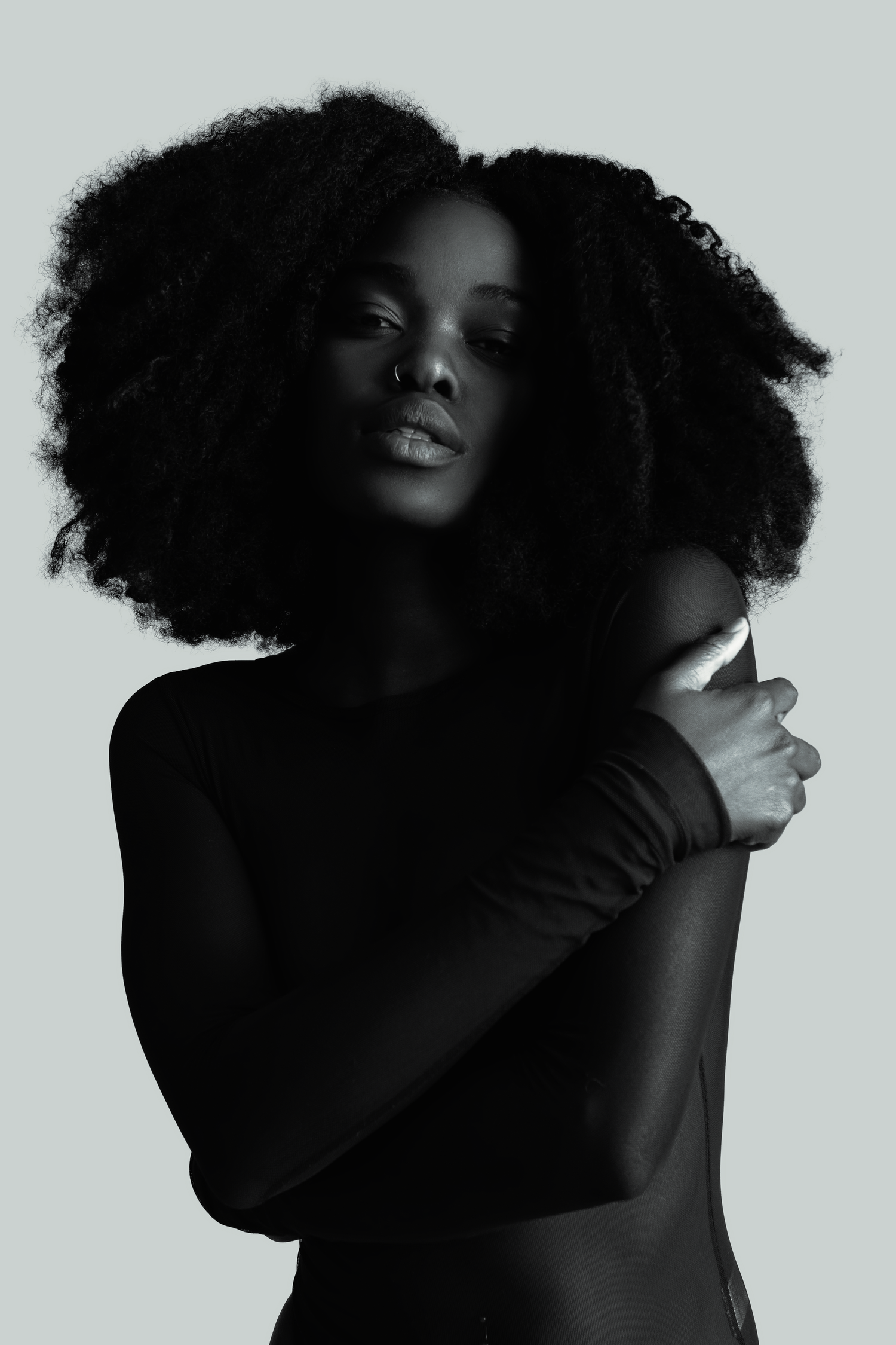 Artistic black and white portrait featuring natural afro hairstyle and elegant pose against light background.