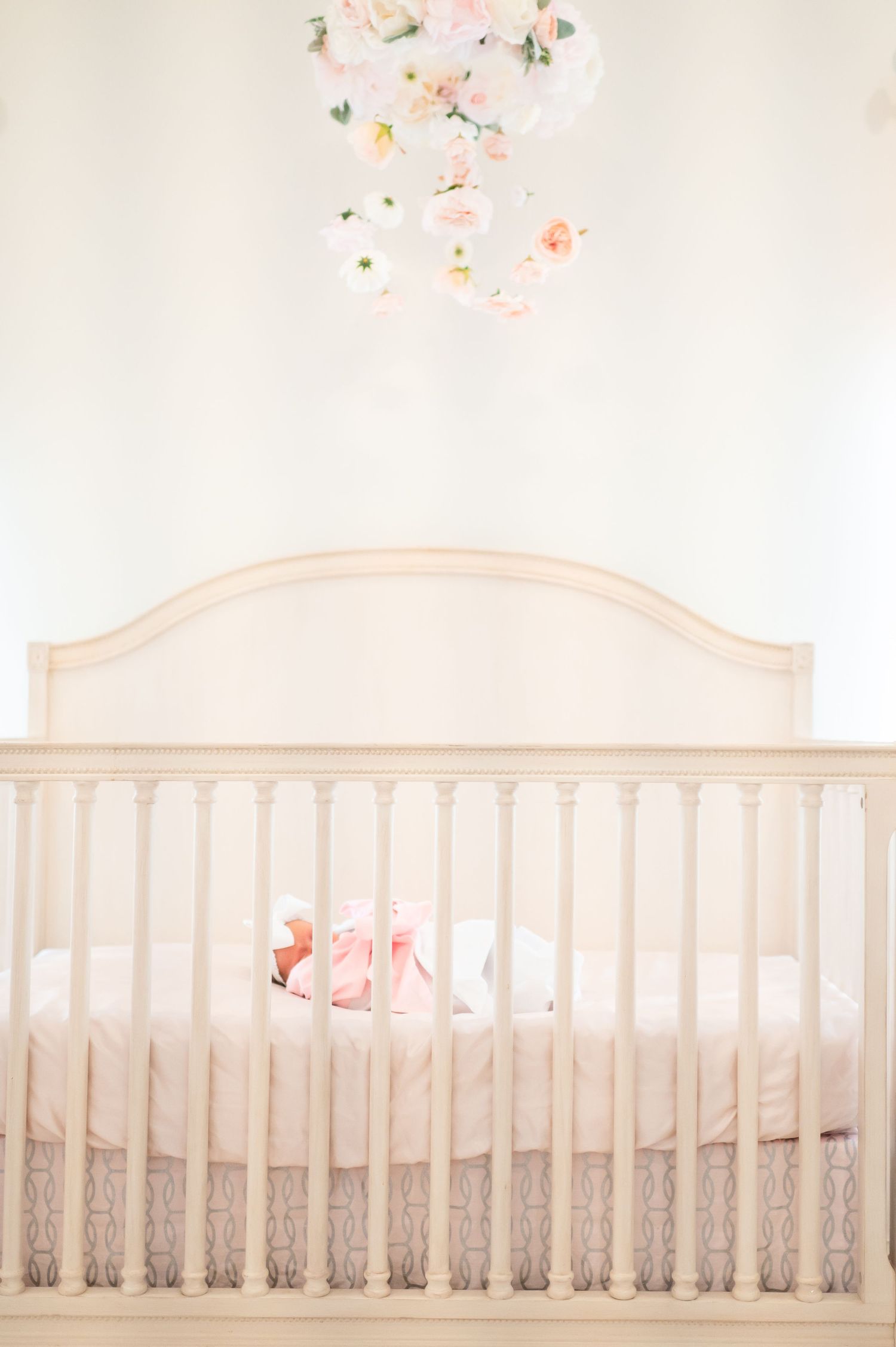beautiful light and airy nursery portrait of a baby girl sleeping in her crib with cascading pink peonies and roses