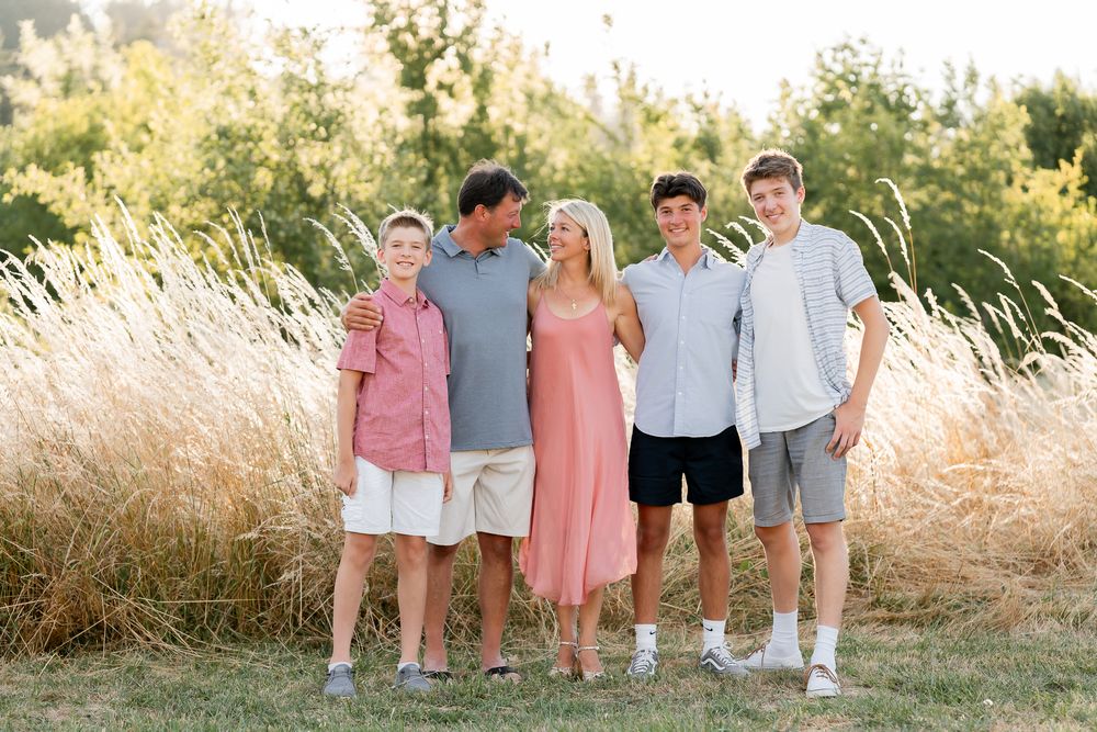 Family photos in casual summer attire standing together outdoors with tall grass in the background.