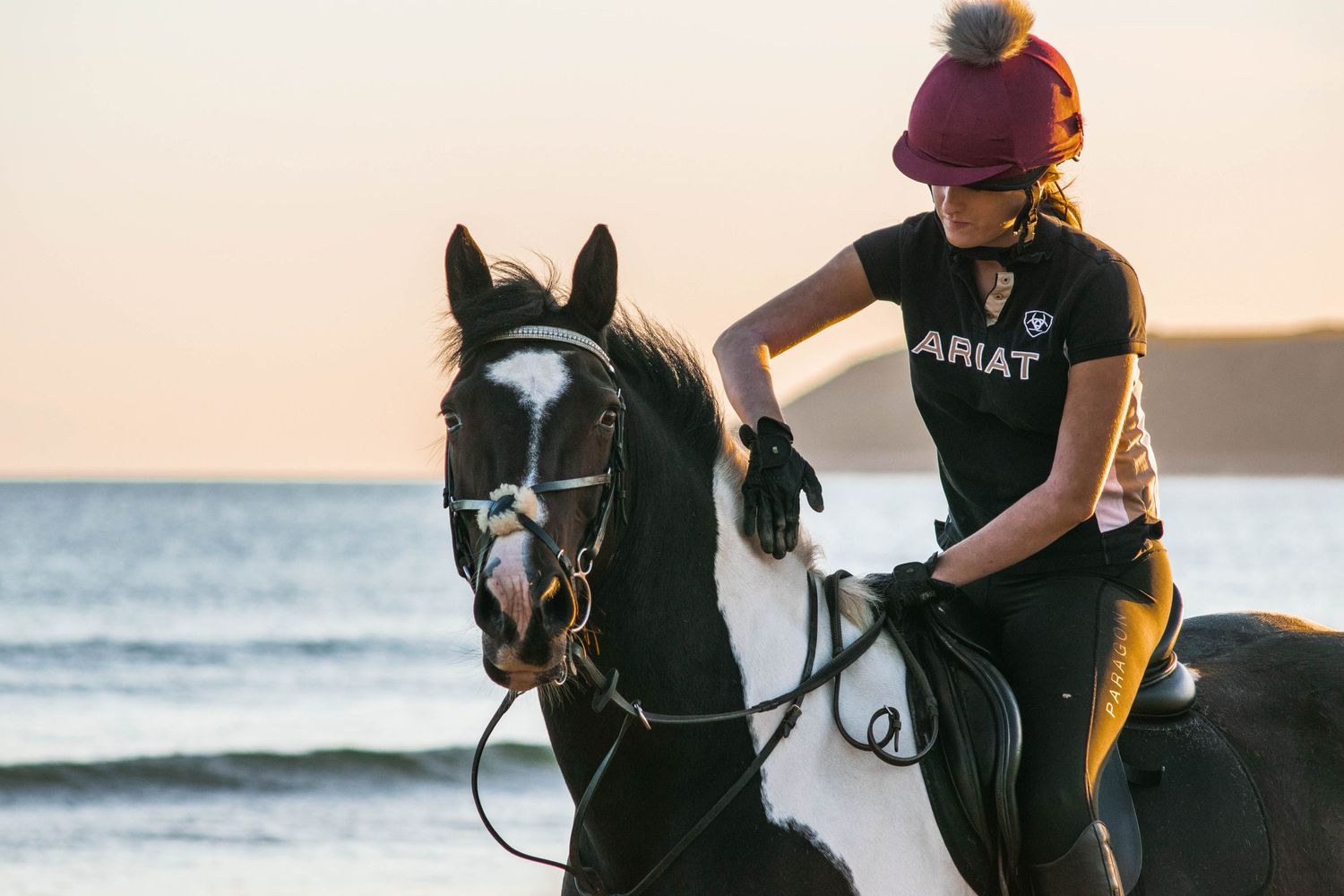 An equestrian rides their horse along a scenic beach at sunset.