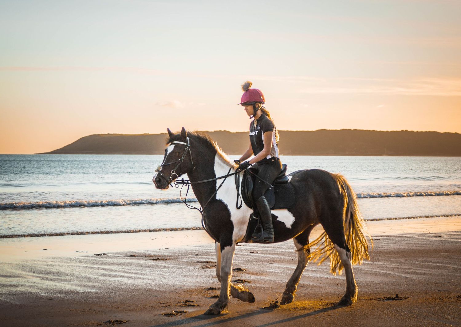 A horse and rider enjoying a peaceful sunset ride along a pristine beach coastline.
