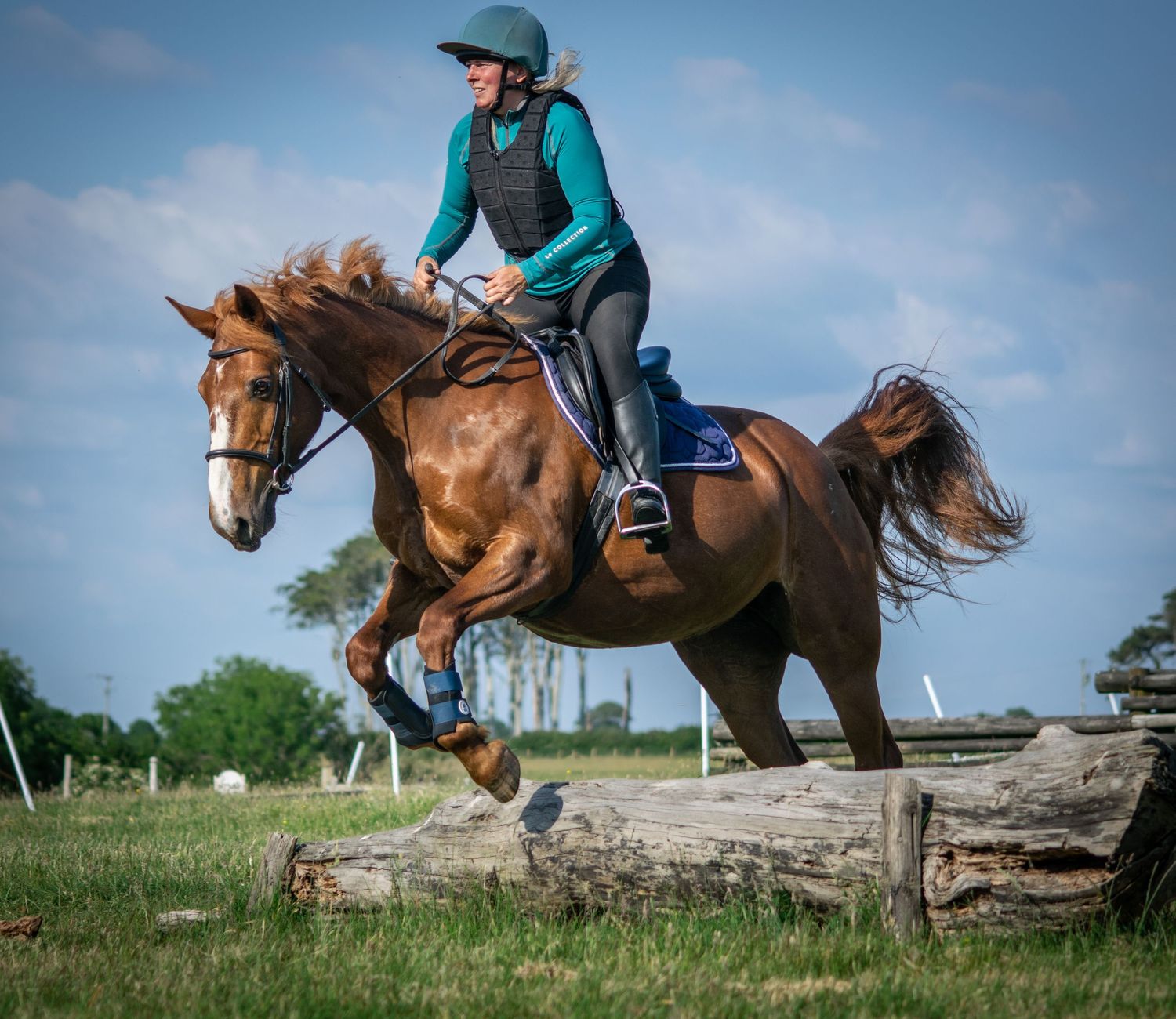 Dynamic sequence of horse and rider jumping over natural rock obstacles against blue sky.