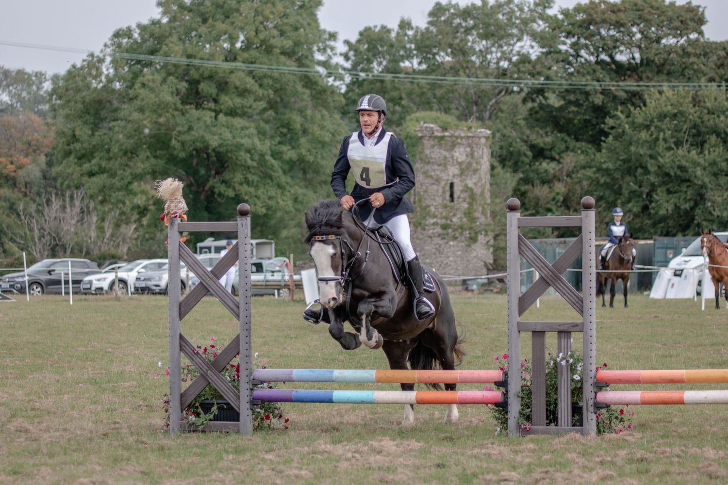 A show jumper clearing a colorful obstacle during an outdoor equestrian competition.
