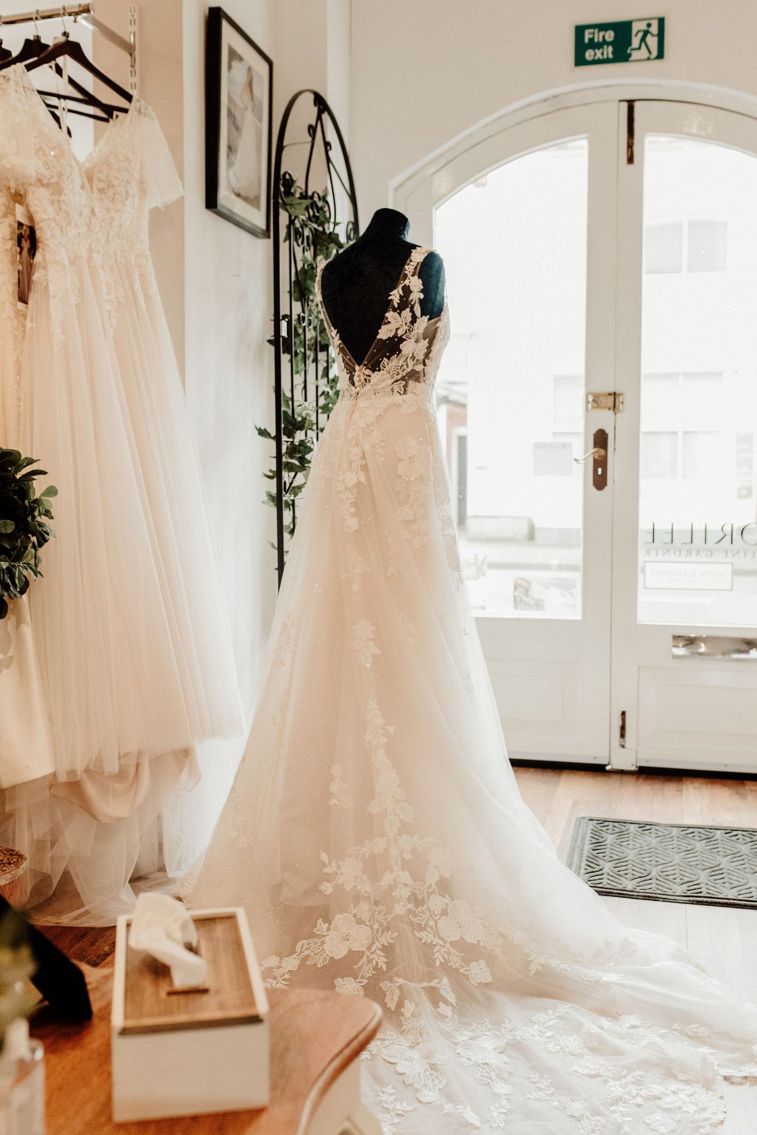 Wedding dress with intricate lace details and long train displayed in bridal boutique window.