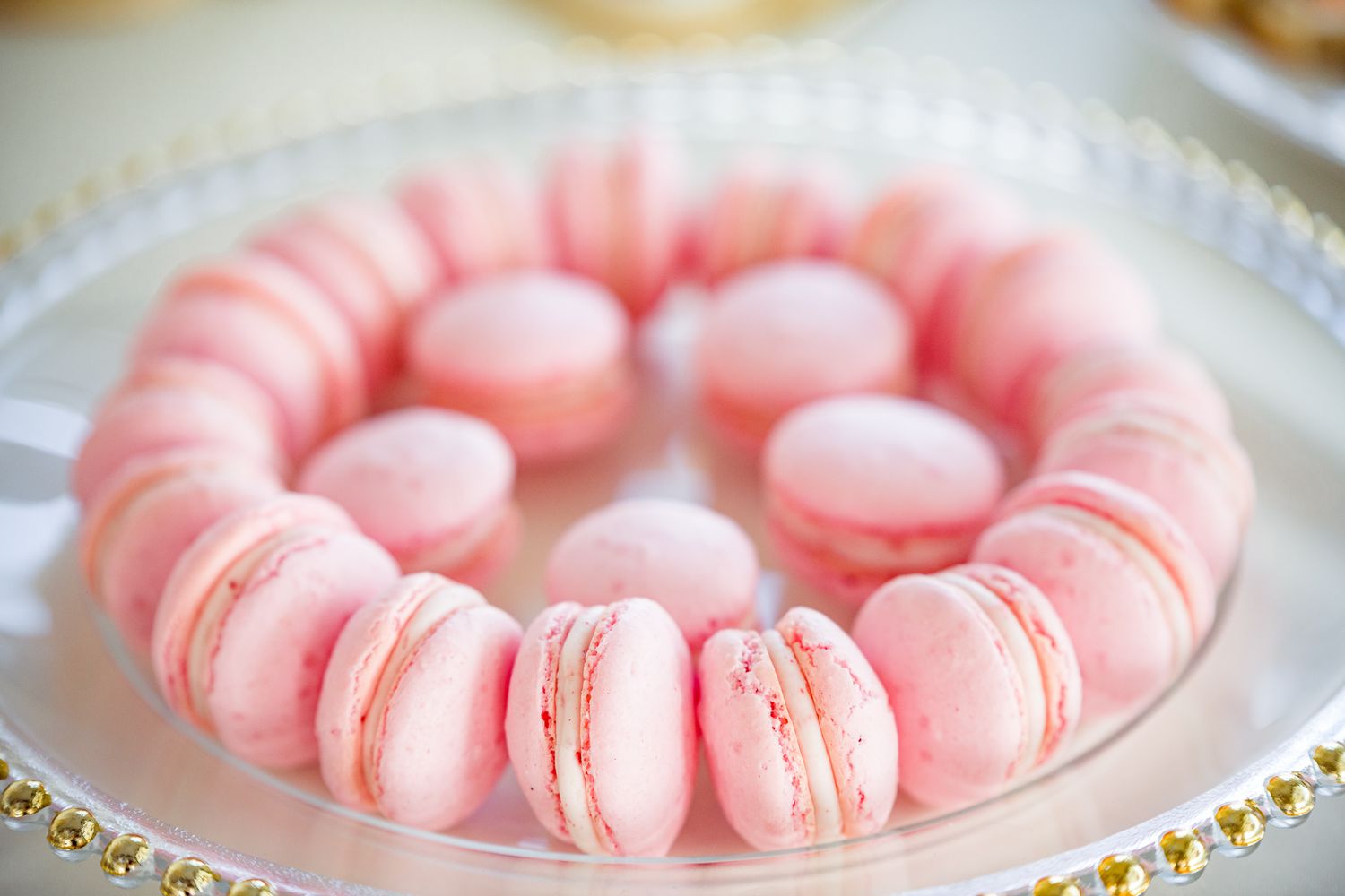Pink French macarons arranged in a circle pattern on a decorative plate with gold trim detail around the edge by Stephanie Coulter Photograp