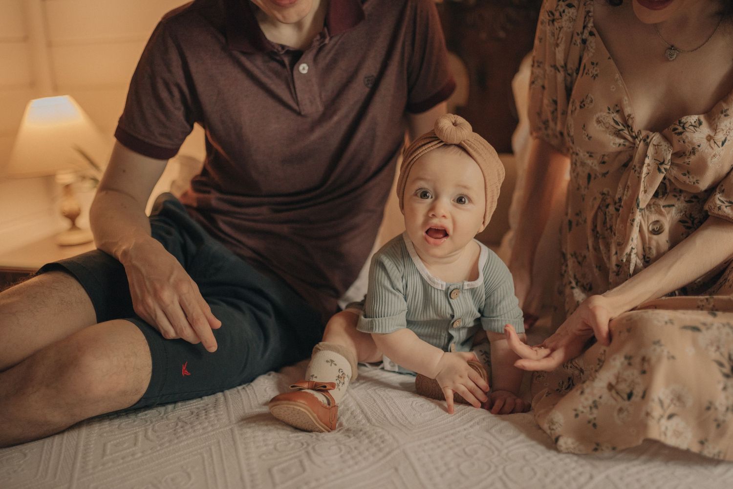 Baby in light blue outfit sitting on bed with family.