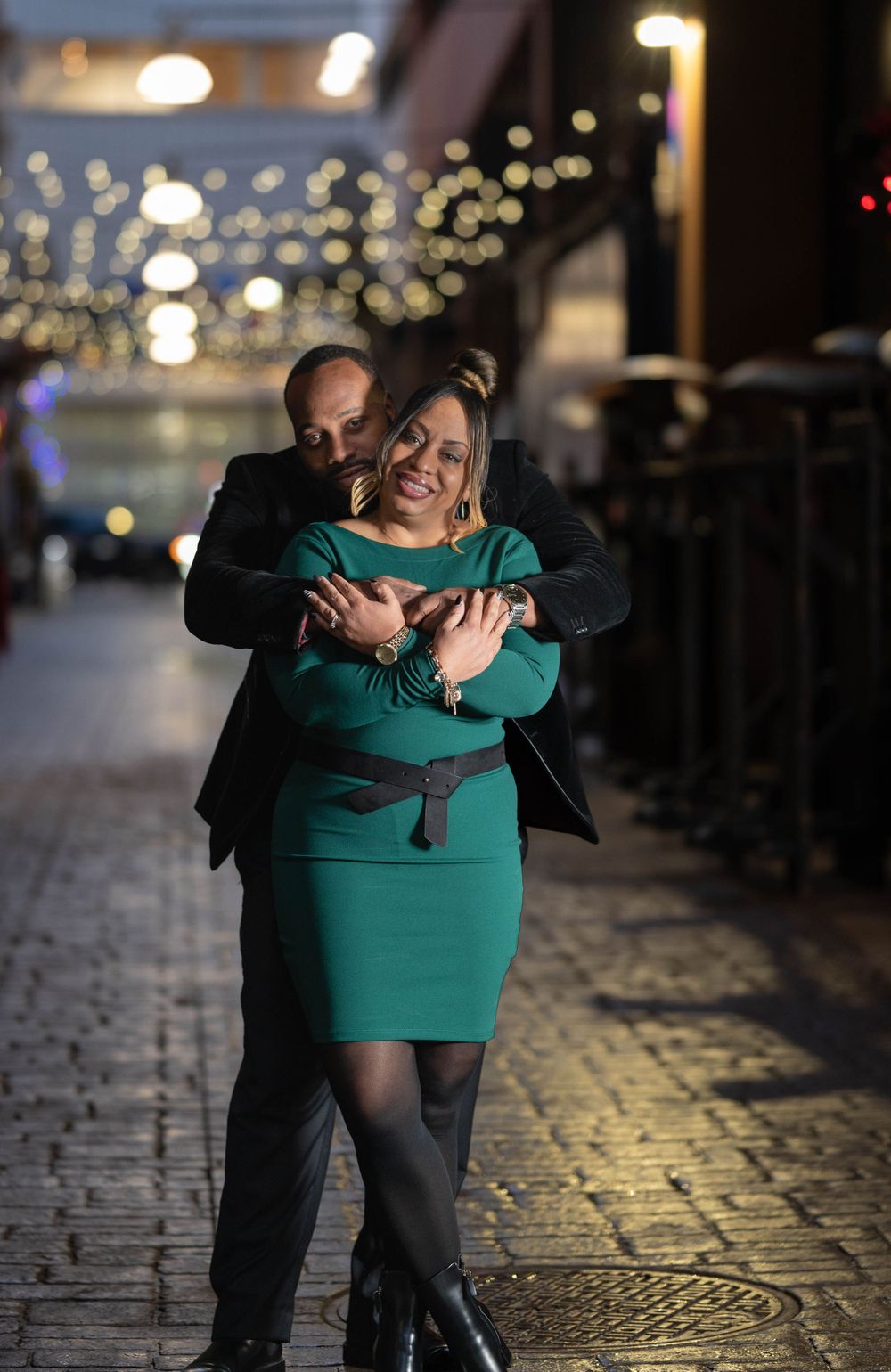 Romantic nighttime portrait with couple embracing under twinkling city lights.