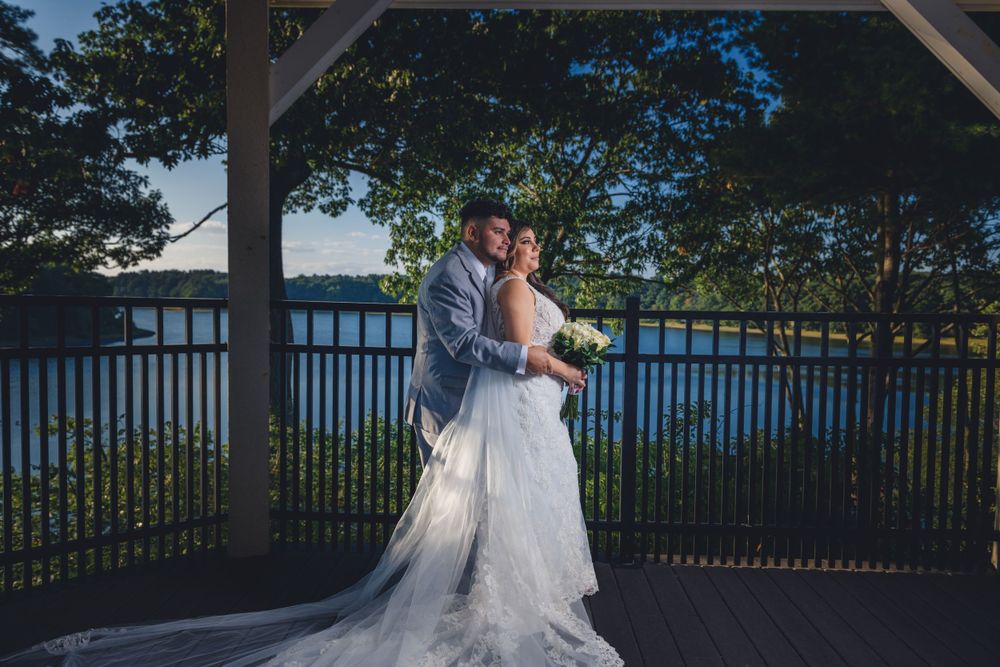 A couple embraces during their waterfront wedding ceremony under a wooden gazebo at sunset.