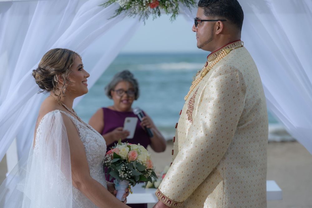 A couple shares a romantic moment during their beach wedding ceremony with tropical ocean backdrop.