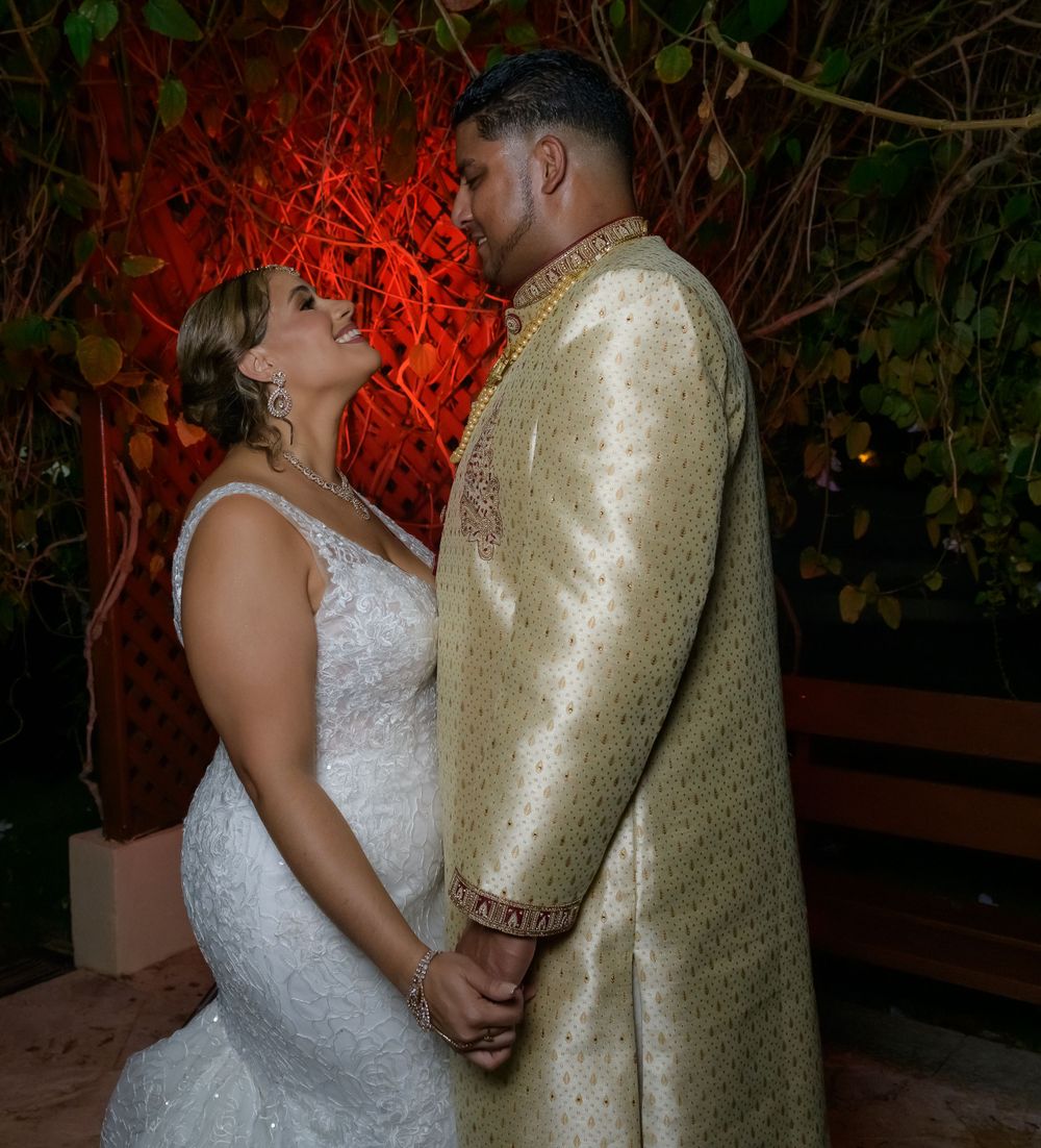 A couple in formal attire share an intimate dance moment under dramatic red lighting at an evening celebration.