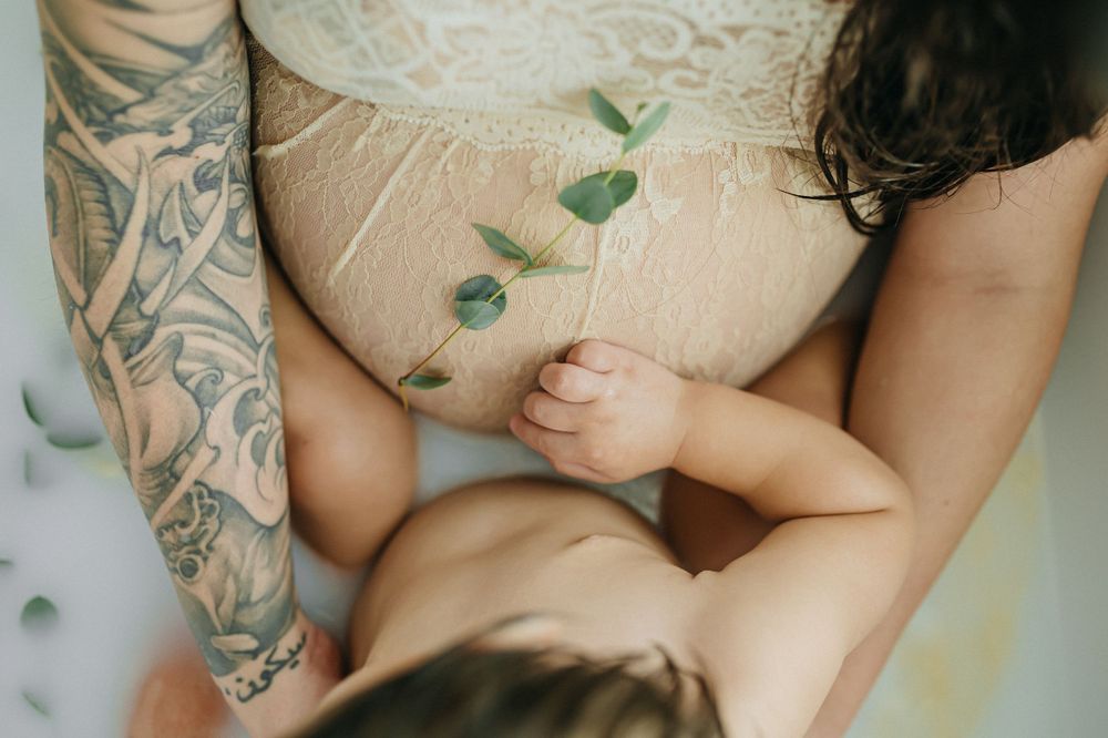 Close-up detail of tattooed arm and lace dress during milk bath photography session.