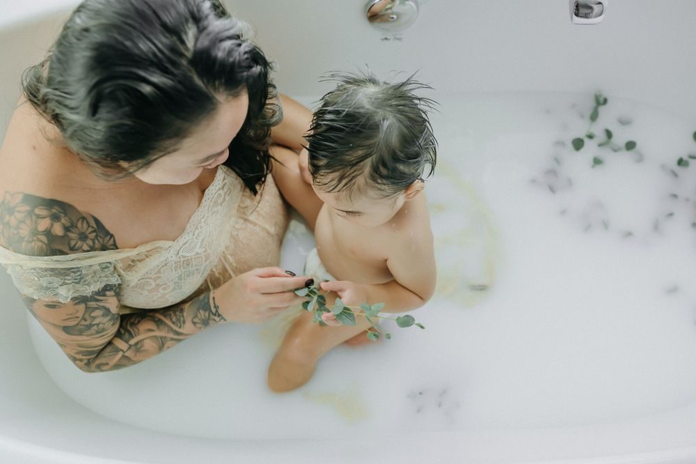 Intimate milk bath photography session featuring eucalyptus leaves floating in milky white water.