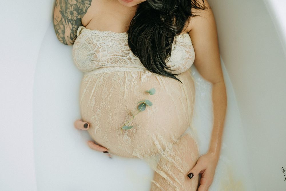 Artistic maternity photo featuring person in cream lace dress with floating eucalyptus leaves.