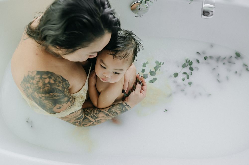 Overhead view of a tender bath moment with floating eucalyptus sprigs in milky water.