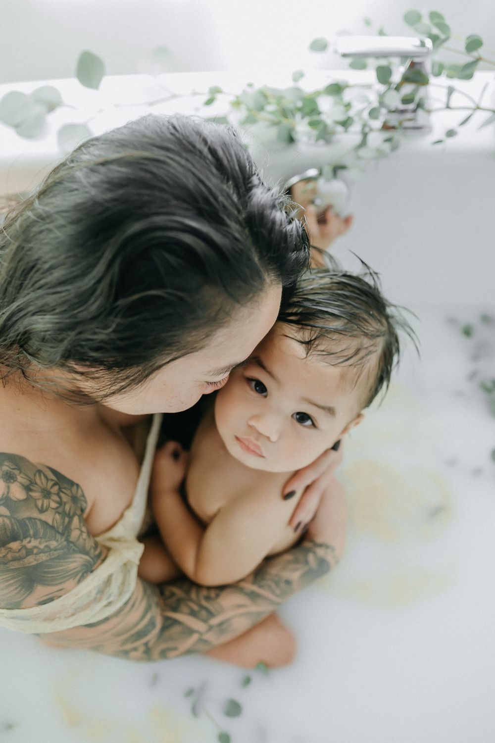 Artistic milk bath portrait with delicate eucalyptus leaves and soft natural lighting.