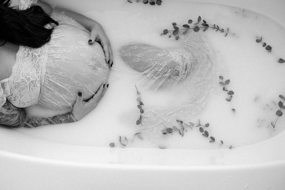 Artistic black and white photo of person in bathtub with floating eucalyptus leaves.