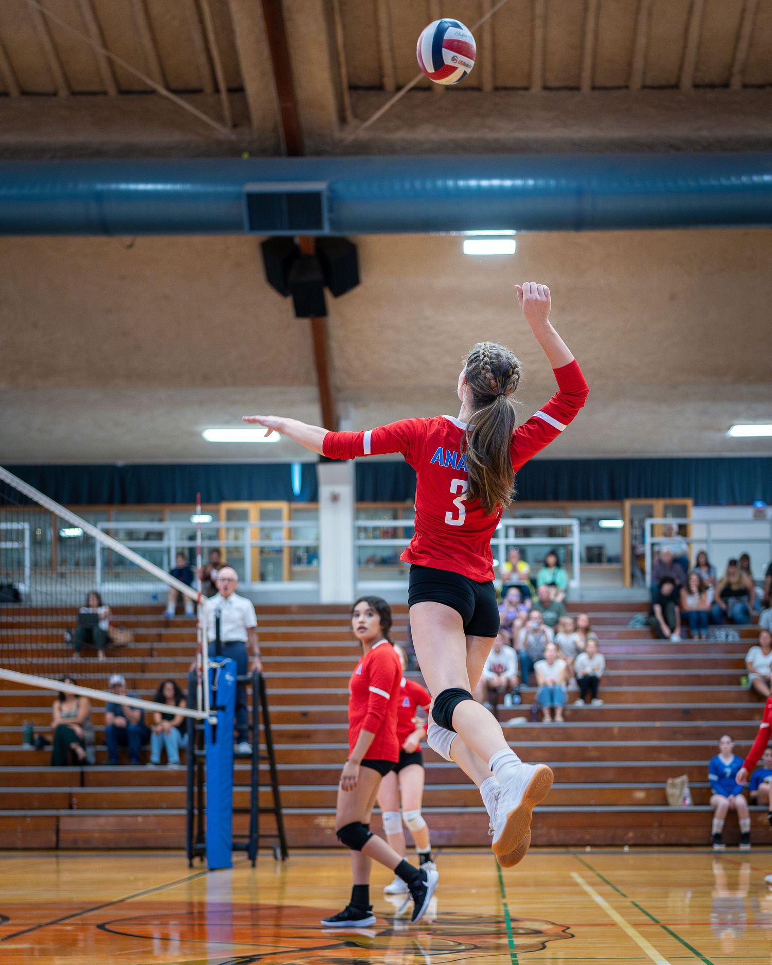 Volleyball player jumps high to spike ball during competitive indoor match on wooden court.