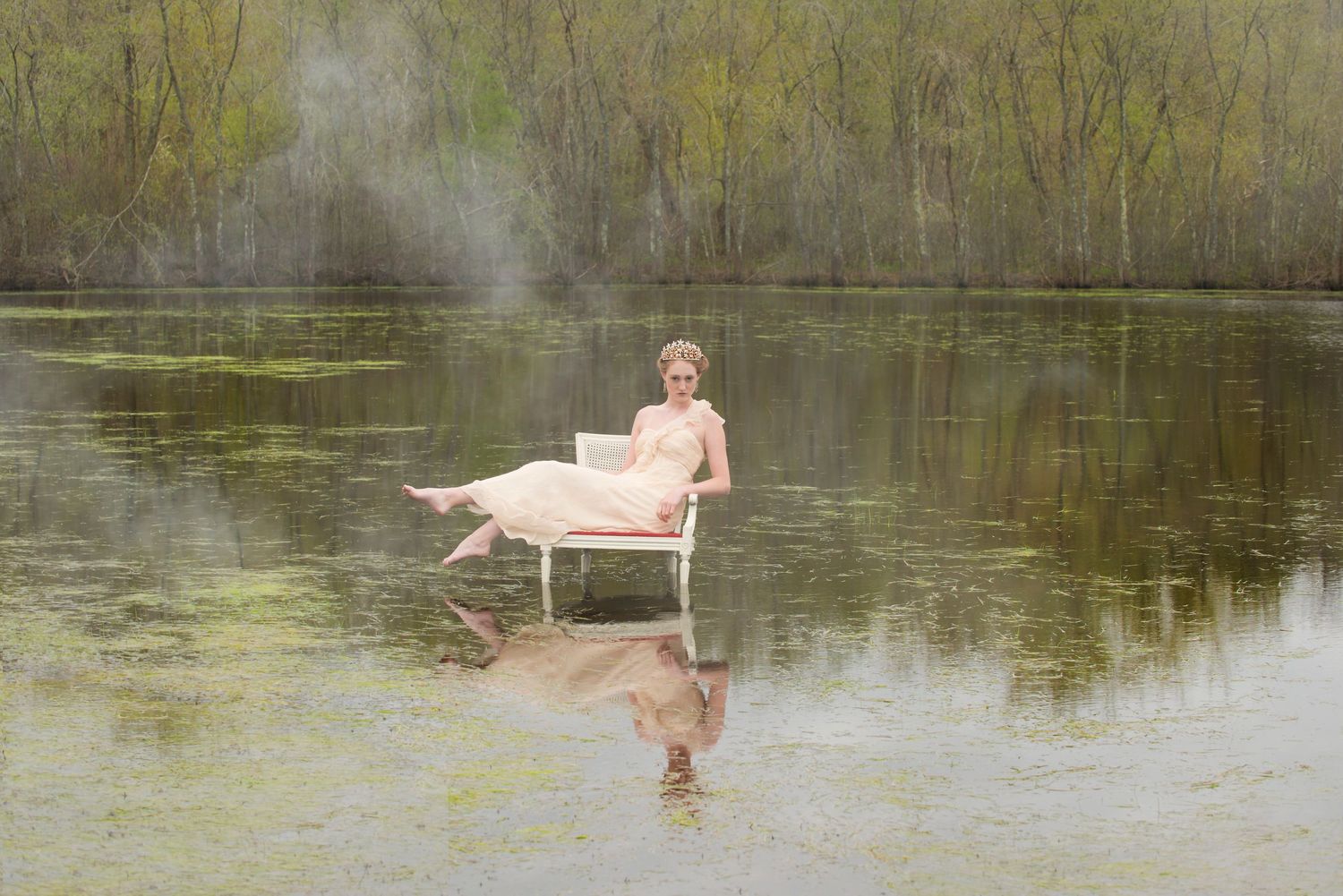 Surreal scene of figure in pink dress sitting on chair in reflective lake water.