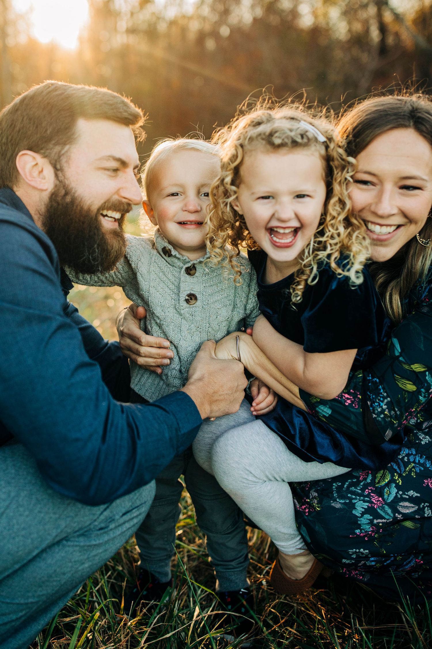 A family shares joyful laughter while sitting together outdoors in golden sunlight.