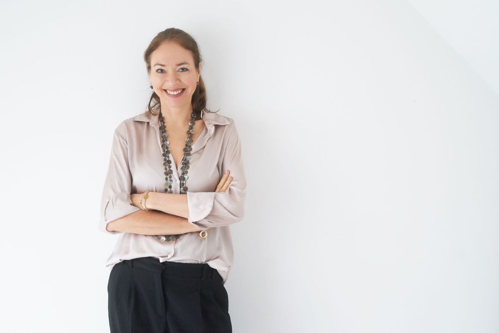 Smiling businesswoman in beige blouse with arms crossed against white background.