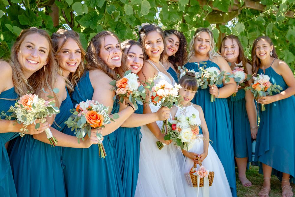 Wedding party members in blue bridesmaid dresses gather together smiling and laughing outdoors.