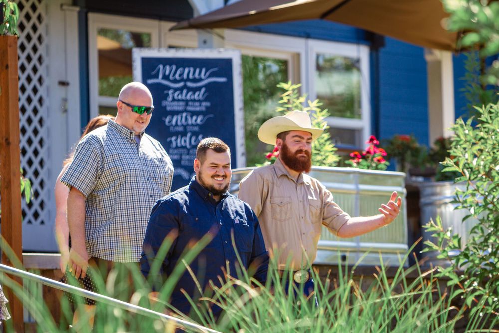 Customers gather outside a blue-painted restaurant with outdoor seating and menu boards on a sunny day.
