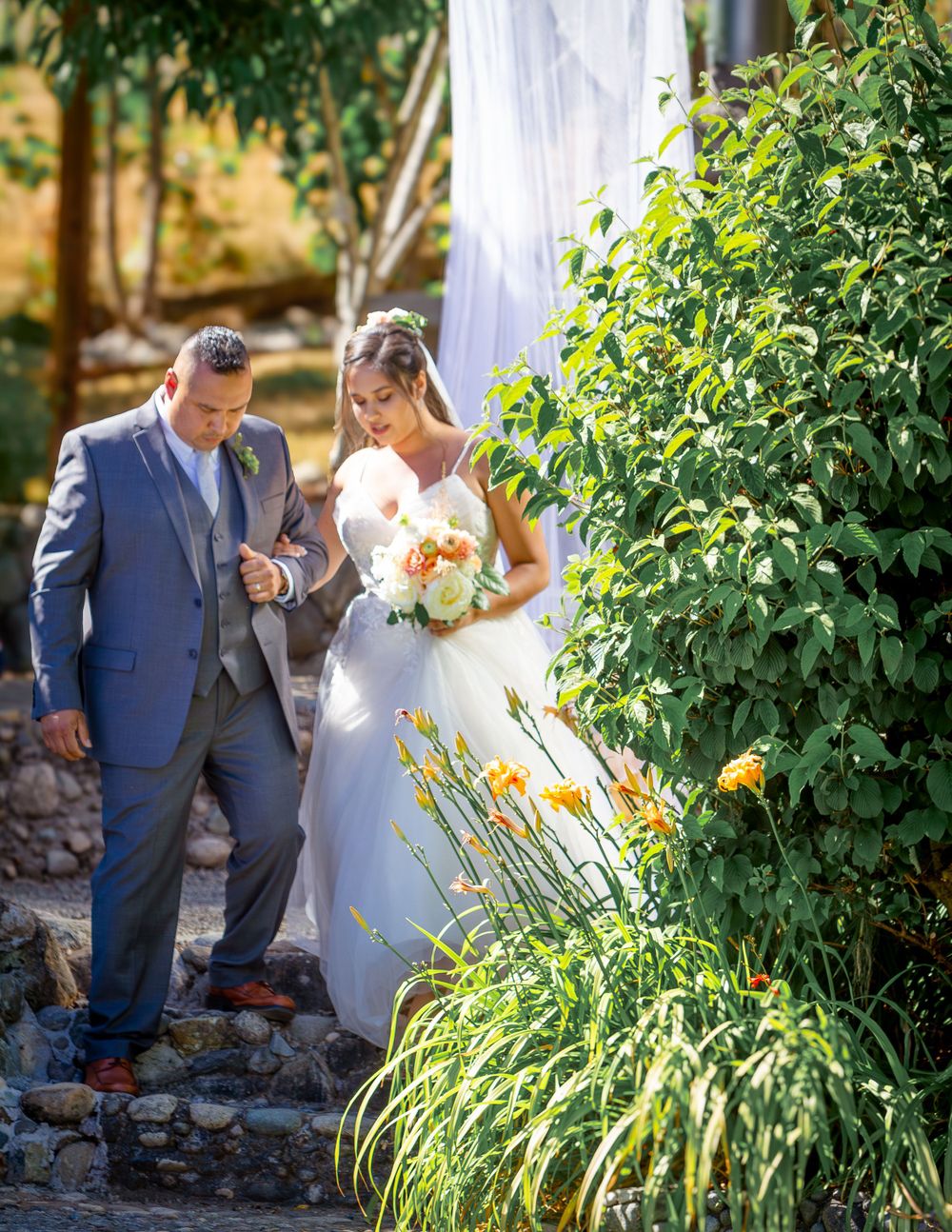 A bride and groom share an intimate moment in a lush garden setting with orange and yellow flowers.