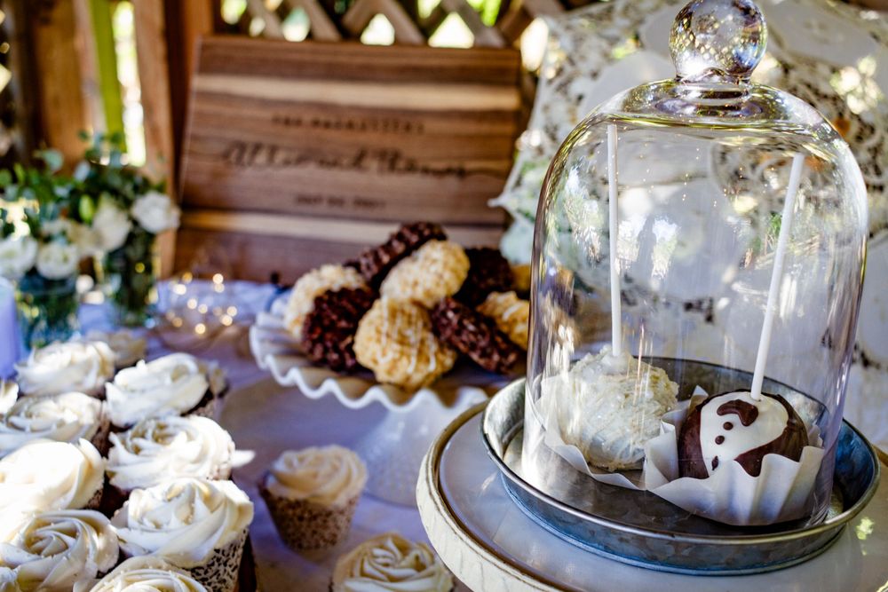 Glass cloches and cake stands display delicate pastries and desserts on a rustic wooden table at an elegant event.
