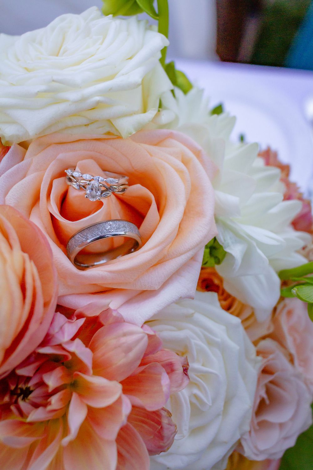 A wedding ring nestled among delicate peach and white roses in a romantic floral arrangement.