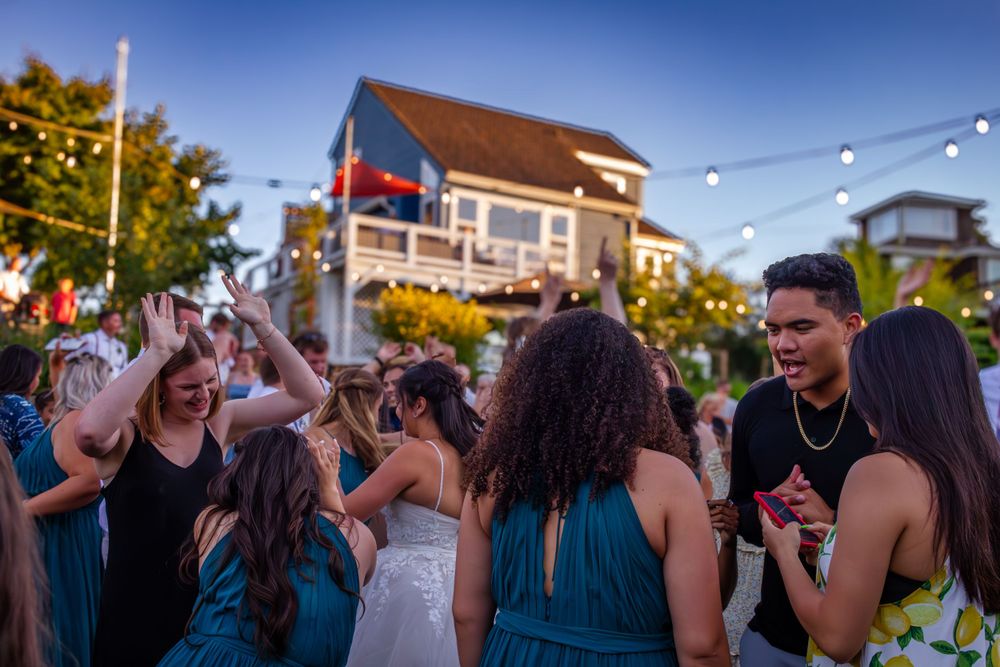 People dancing and socializing outdoors at a summer party with string lights and buildings in the background.