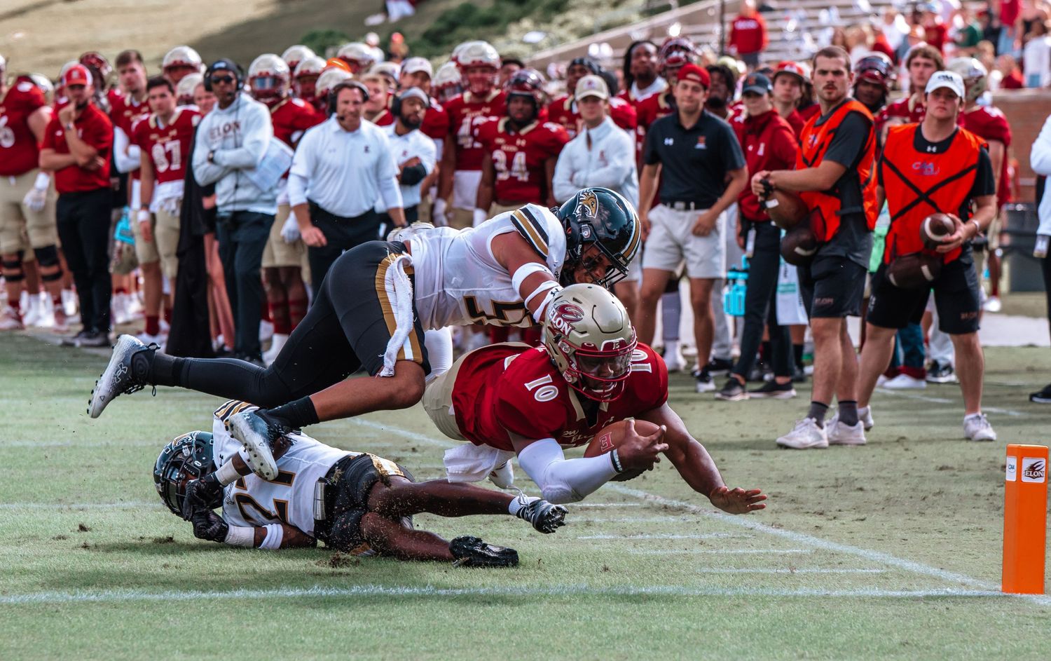 Football players collide during an intense tackle play near the sidelines of a crowded stadium.