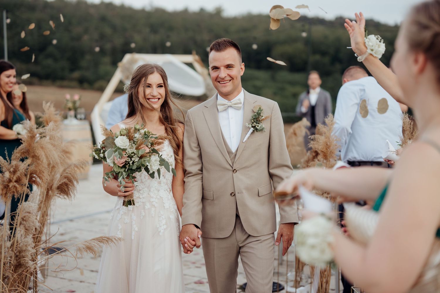Newlyweds walking through confetti on a rustic outdoor path at sunset.